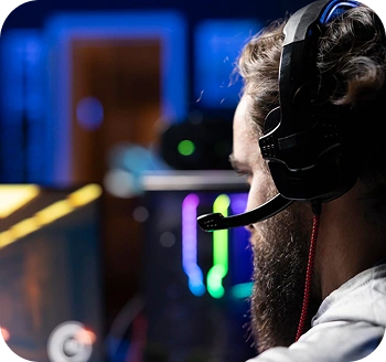 Widok z boku profesjonalnego gracza e-sportowego z zestawem słuchawkowym, skupionego na meczu konkurencyjnym w gamingowej konfiguracji z oświetleniem RGB.