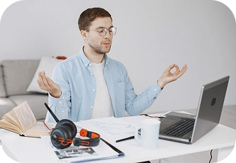 Młody mężczyzna medytujący przy biurku, studiujący na laptopie, koncentrując się i kontrolując stres podczas nauki online.