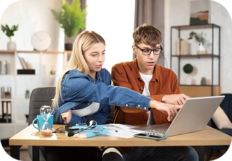 Dwóch studentów współpracujących w domu przy laptopie, omawiających swoje zadania domowe i pracujących razem nad projektem studenckim.